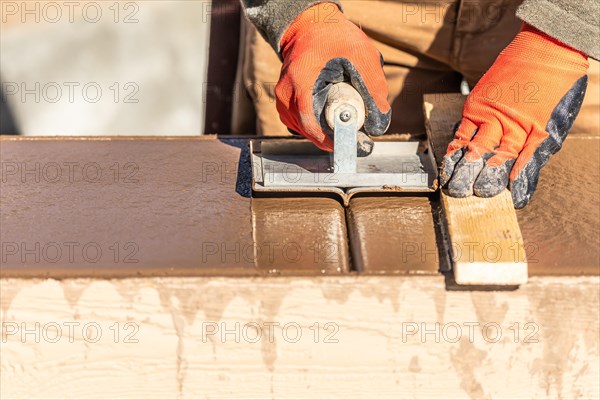 Construction worker using hand groover on wet cement forming coping around new pool