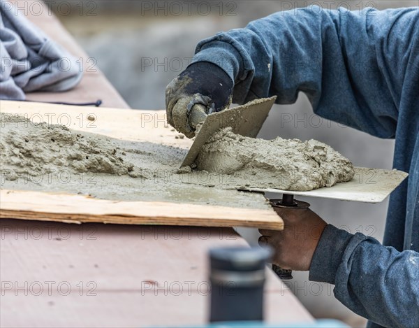 Tile worker mixing wet cement on board at pool construction site