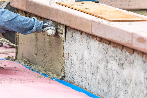 Tile worker applying cement with trowel at pool construction site