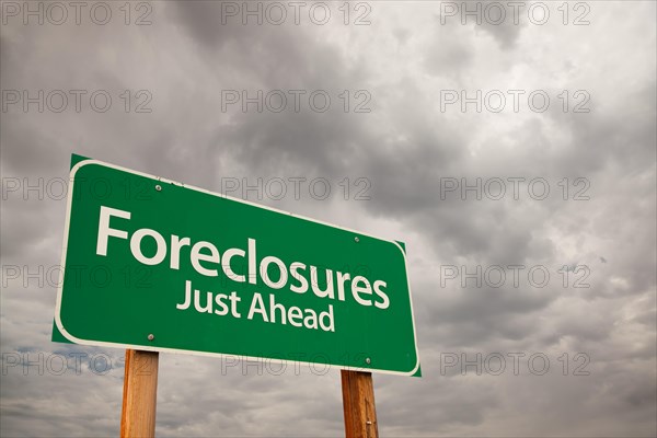 Foreclosures just ahead green road sign with dramatic storm clouds and sky