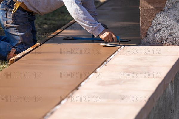 Construction worker smoothing wet cement with hand edger tool