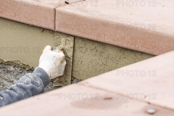 Tile worker applying cement with trowel at pool construction site