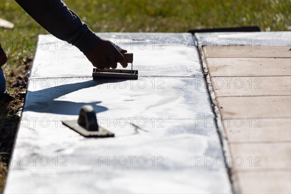 Construction worker smoothing wet cement with hand edger tool