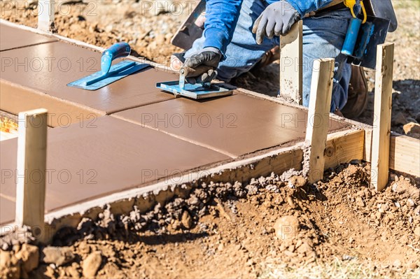 Construction worker using hand groover on wet cement forming coping around new pool