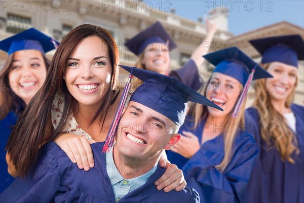 Proud male graduate in cap and gown with girl among other graduates behind