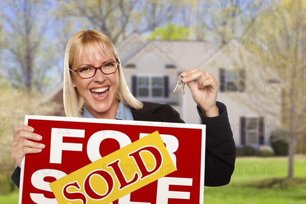 Happy young woman with sold for sale real estate sign and keys in front of house