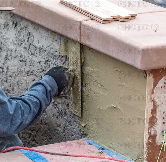 Tile worker applying cement with trowel at pool construction site