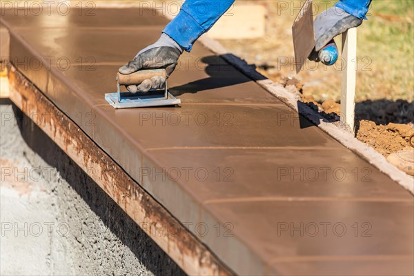 Construction worker using hand groover on wet cement forming coping around new pool