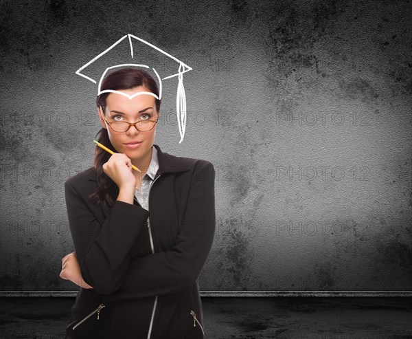 Graduation cap drawn on head of young adult woman with pencil in front of wall with copy space