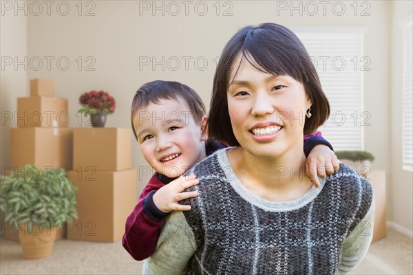 Chinese mother and mixed-race child inside empty room with moving boxes and plants