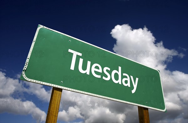 Tuesday green road sign with dramatic blue sky and clouds