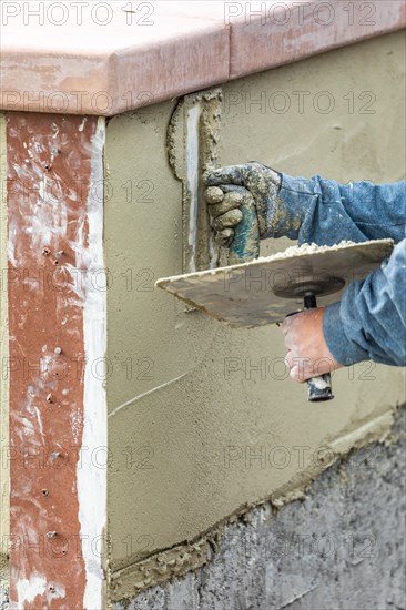 Tile worker applying cement with trowel at pool construction site