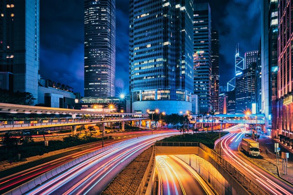 Street traffic in Hong Kong at night. Office skyscraper buildings and busy traffic on highway road with blurred cars light trails. Hong Kong