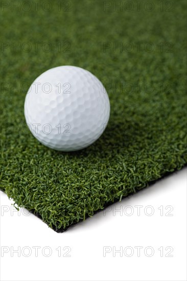 Golf ball resting on section of artificial turf grass on white background