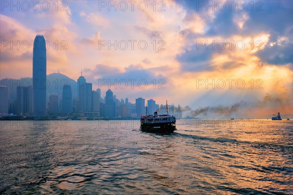 Hong Kong skyline cityscape downtown skyscrapers over Victoria Harbour on sunset with tourist ferry boat silhouette