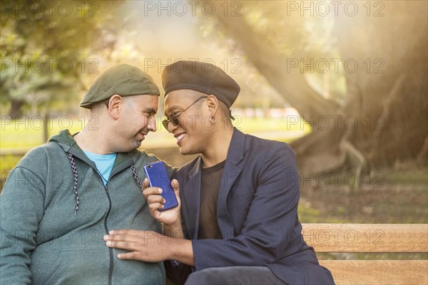 Gay Latino male couple sitting on a bench in a park at sunset
