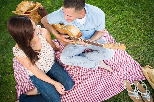 Young adult man playing guitar for his girlfriend in the park