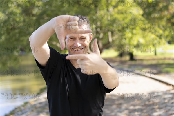 A handsome mature man looks through a frame made up of hands. Attractive man make frame by fingers