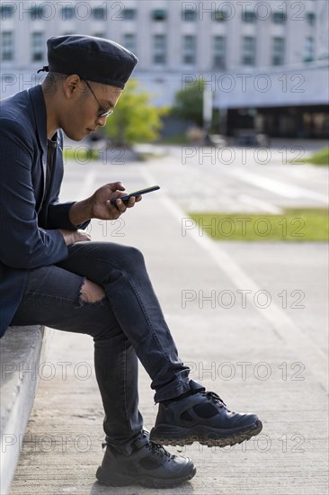 Latino gay male with makeup on wearing trendy hat looking at cell phone in a park