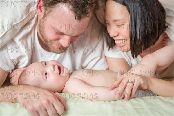mixed-race chinese and caucasian baby boy laying in bed with his father and mother