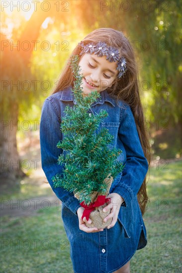 Cute mixed-race young girl holding small christmas tree outdoors