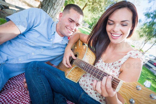 Young adult girl playing guitar with boyfriend in the park