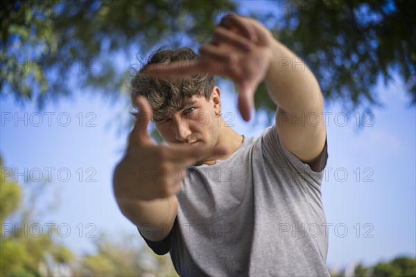 A handsome young man blinks his eyes and looks through a frame made up of hands. Attractive man make frame by fingers