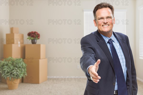 Smiling businessman reaching for a hand shake in empty room with packed boxes