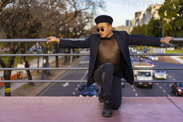 Latino gay male with makeup wearing trendy hat posing on a bridge