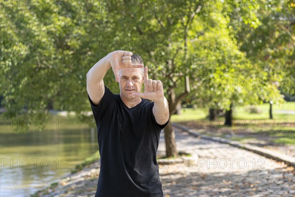 A handsome mature man looks through a frame made up of hands. Attractive man make frame by fingers