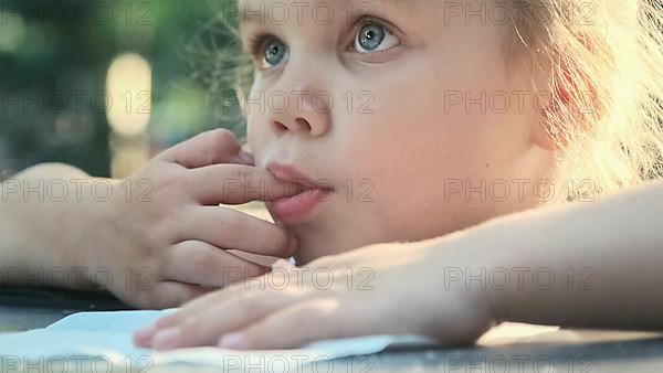 Little girl tastes salt. Close-up portrait of blonde girl takes salt from napkin with her finger and tastes it while sitting in street cafe on the park. Odessa