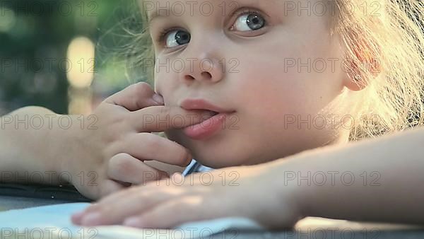 Little girl tastes salt. Close-up portrait of blonde girl takes salt from napkin with her finger and tastes it while sitting in street cafe on the park. Odessa Ukraine