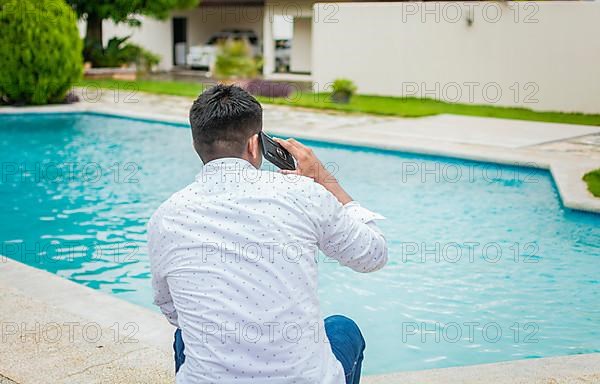 Handsome man sitting calling on the phone near the swimming pool