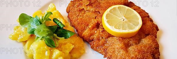 Delicious golden-brown fried Wiener Schnitzel with potato salad and a slice of lemon on a white plate,