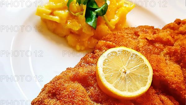 Delicious golden-brown fried Wiener Schnitzel with potato salad and a slice of lemon on a white plate,