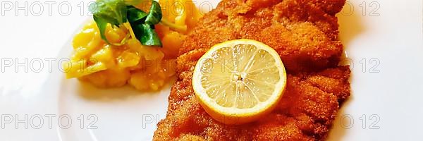 Delicious golden-brown fried Wiener Schnitzel with potato salad and a slice of lemon on a white plate,