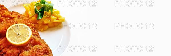 Delicious golden-brown fried Wiener Schnitzel with potato salad and a slice of lemon on a white plate,