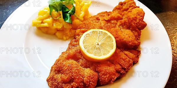 Delicious golden-brown fried Wiener Schnitzel with potato salad and a slice of lemon on a white plate,