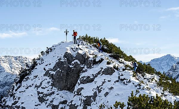 Mountaineers at the summit cross of the Weitalpspitz in winter with snow, Ammergau Alps