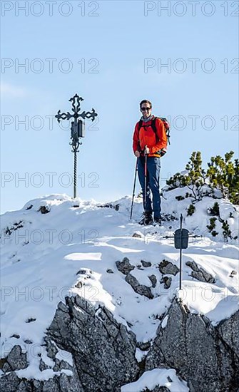 Mountaineer next to summit cross of Weitalpspitz in winter with snow, Ammergau Alps