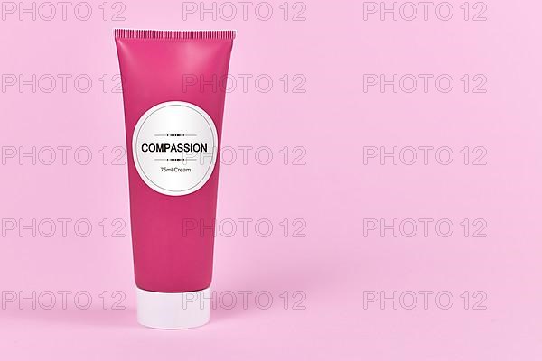 Compassion concept with cream tube with made up label saying Compassion, 75ml cream on pink background with blank copy space