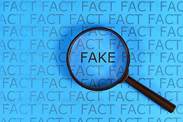 Concept for Fake News with words fact in row and single word fake highlighted by magnifying glass on blue background,