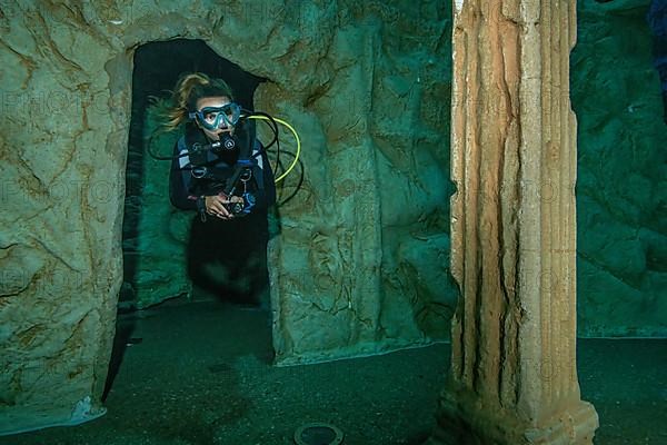 Diver dives through small gate of stylised ruin of ancient temple in 20 metres depth in indoor diving tower