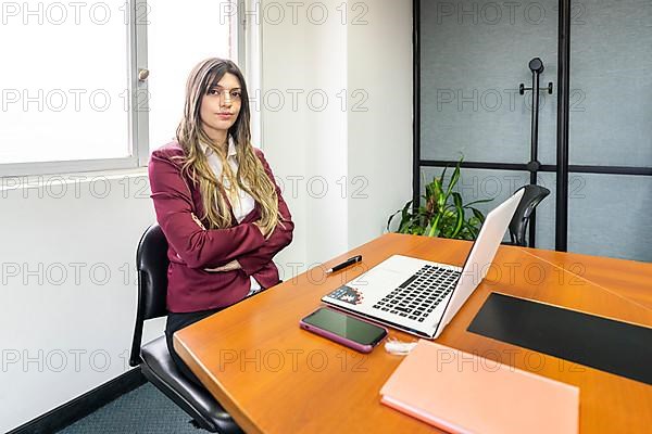 Young blonde businesswoman sitting with her arms crossed at the head of the table in the office meeting room