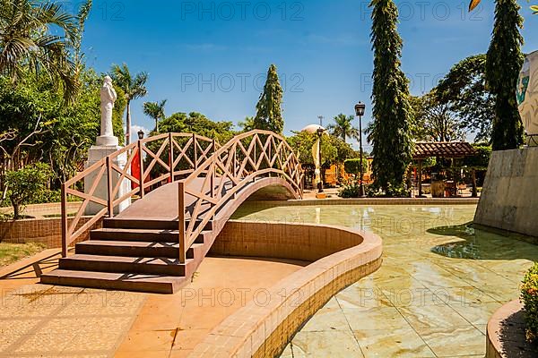 View of a calm park with a small wooden bridge over a water fountain. Nagarote central park. Image of a nice and relaxed park with a water fountain surrounded by trees. Traditional park of Nagarote