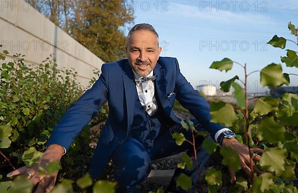 Man in blue suit hiding behind bushes