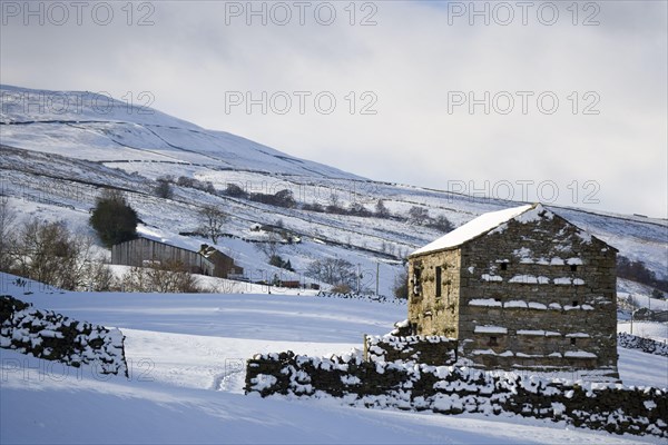 View of snow covered upland farmland with stone barn and drystone walls