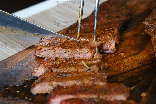 Cutting juicy grilled top blade beefsteak on wooden cutting board