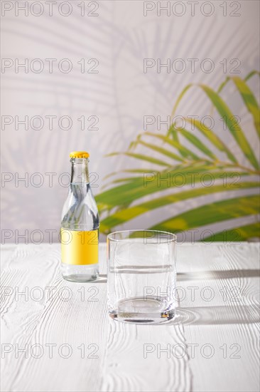 Empty glass on the table and small bottle of tonic water in background under morning sunlight