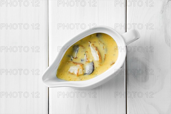 Mushroom sauce in ceramic gravy boat on white wooden table